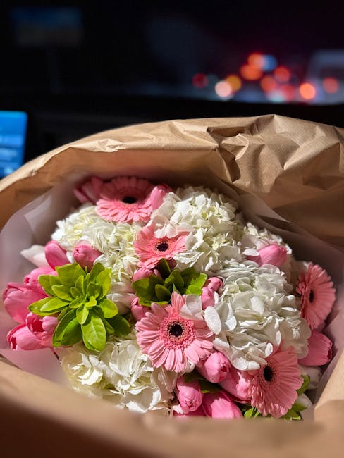A bouquet of fresh flowers featuring pink gerbera daisies with black centers, white hydrangeas with clustered petals, and bright green succulents, arranged in a natural, slightly dispersed manner. The